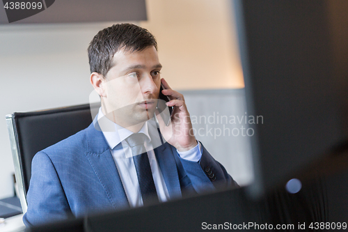 Image of Businessman talking on mobile phone while watching charts and data analyses on multiple computer screens.