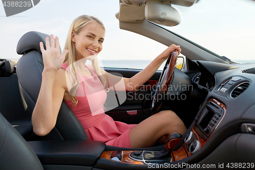 Image of happy young woman in convertible car waving hand