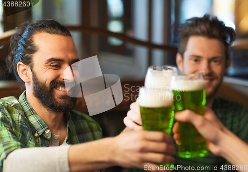 Image of male friends drinking green beer at bar or pub