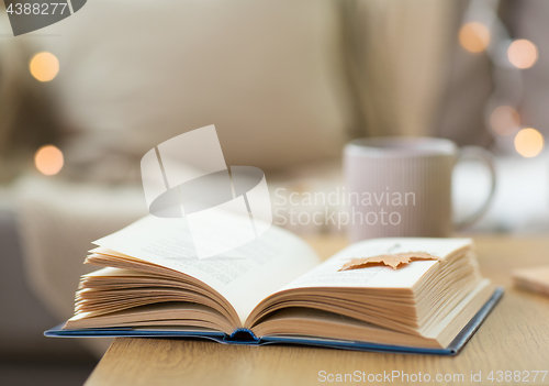 Image of book with autumn leaf on wooden table at home