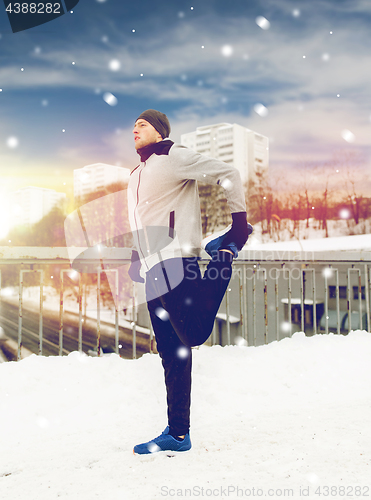 Image of man exercising and stretching leg on winter bridge