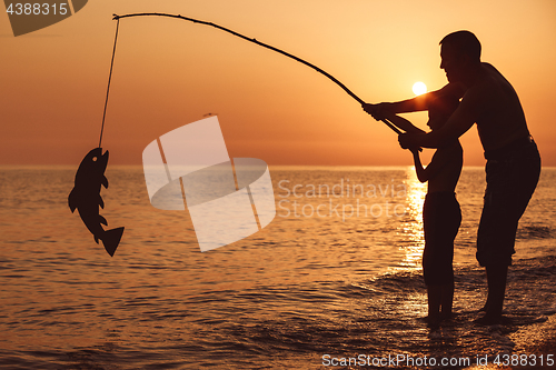 Image of Father and son  playing on the beach at the sunset time.