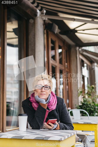 Image of Dreamy woman with phone in cafe