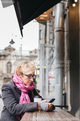 Image of Woman browsing smartphone in outside cafe