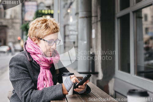 Image of Woman browsing smartphone in outside cafe