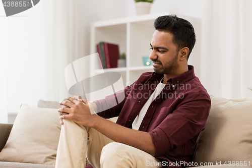 Image of unhappy man suffering from pain in leg at home