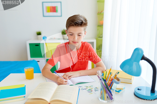 Image of student boy in earphones writing to notebook