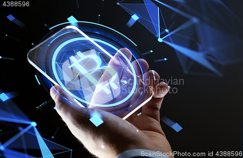 Image of close up of hand with smartphone and bitcoin