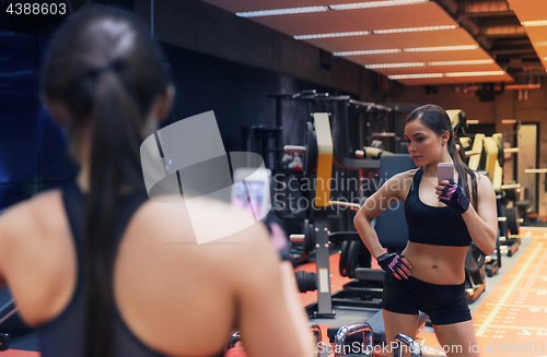 Image of woman with smartphone taking mirror selfie in gym