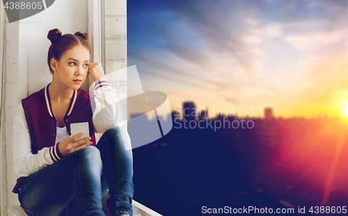 Image of teenage girl sitting on windowsill with smartphone