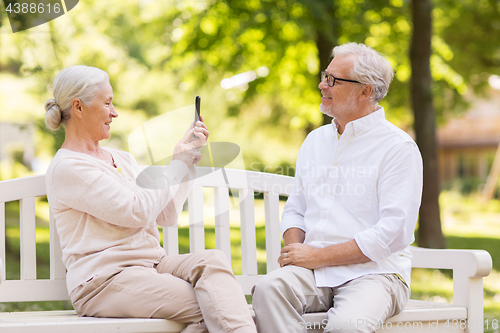 Image of old woman photographing man by smartphone in park