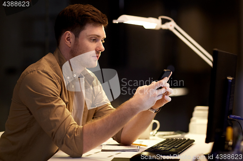 Image of man with smartphone working late at night office