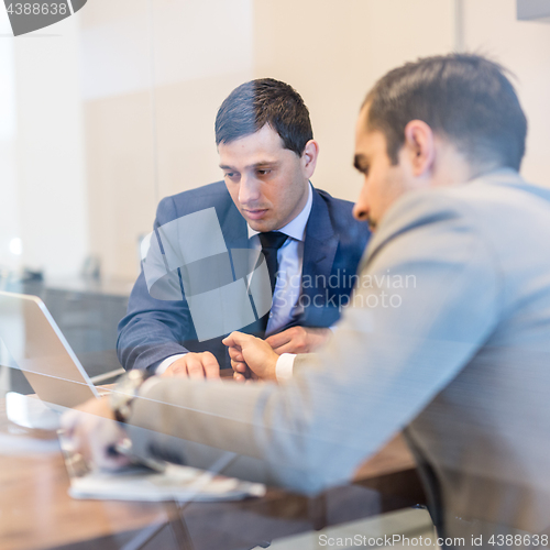 Image of Two young businessmen using laptop computer at business meeting.