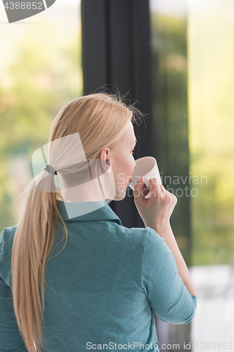 Image of young woman drinking morning coffee by the window