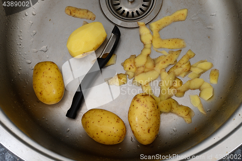 Image of vegetable peeler, potatoes and potato peelings in the sink