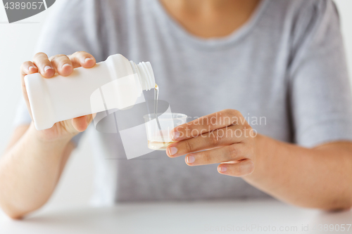 Image of woman pouring syrup from bottle to medicine cup