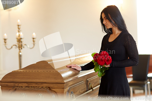 Image of sad woman with red rose and coffin at funeral