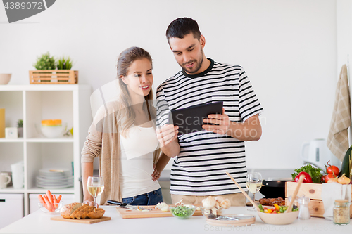 Image of happy couple with tablet pc cooking food at home