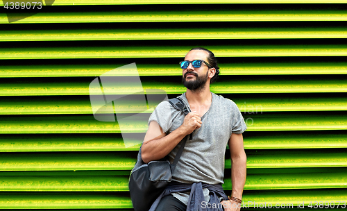 Image of man in sunglasses with bag standing at street wall