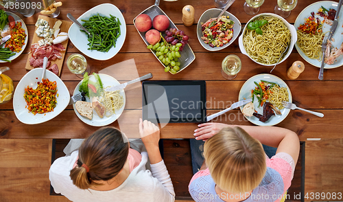 Image of women with tablet pc at table full of food