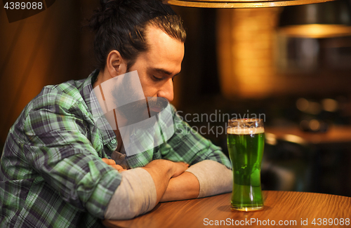 Image of lonely man drinking green beer at bar or pub