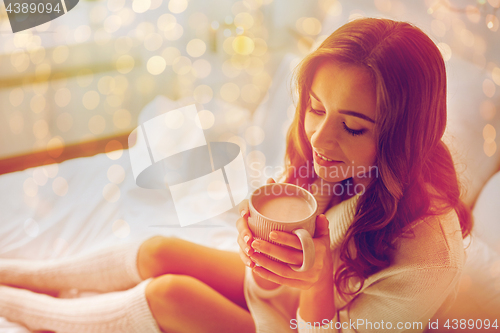 Image of happy woman with cup of cocoa in bed at home