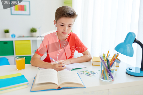 Image of student boy in earphones writing to notebook