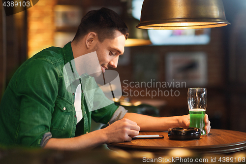 Image of man with smartphone and green beer texting at bar