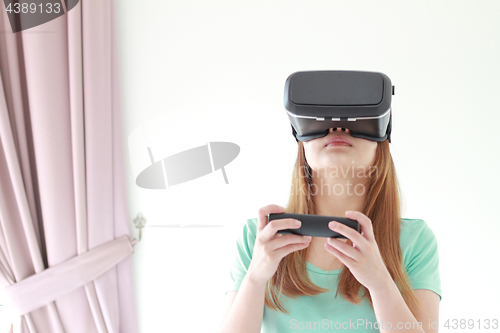 Image of Young woman wearing virtual reality glasses at home.