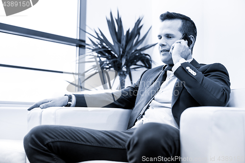 Image of Low angle shot of a handsome young businessman in a stylish modern office space with large windows, talking on mobile phone.