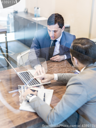 Image of Two young businessmen using laptop computer at business meeting.