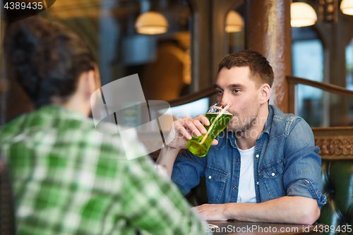 Image of male friends drinking green beer at bar or pub