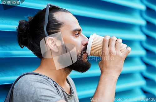 Image of man drinking coffee from paper cup over wall