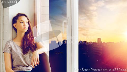 Image of sad pretty teenage girl sitting on windowsill