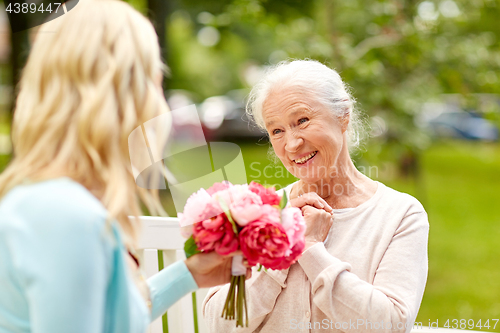 Image of daughter giving flowers to senior mother at park