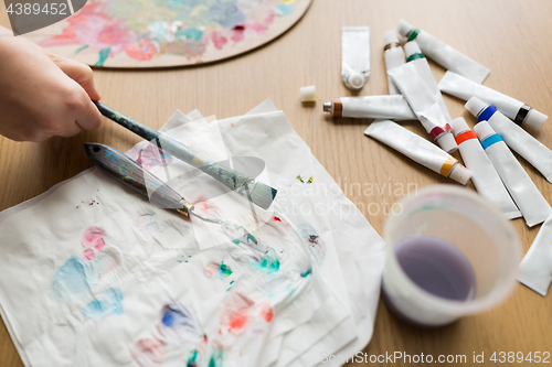 Image of artist hand with paintbrush, paper and paint tubes