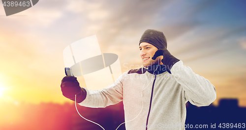Image of happy man with earphones and smartphone in winter