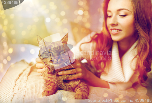 Image of happy young woman with cat lying in bed at home