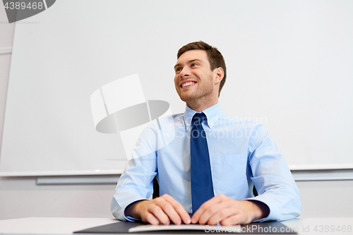 Image of smiling young businessman sitting at office table