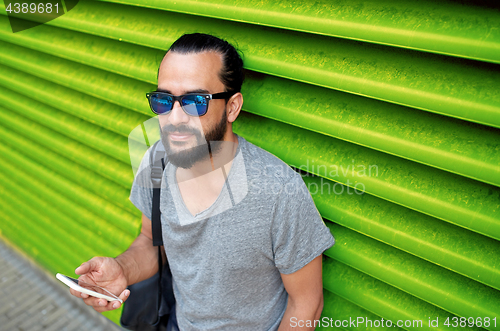 Image of man in sunglasses with smartphone and bag at wall