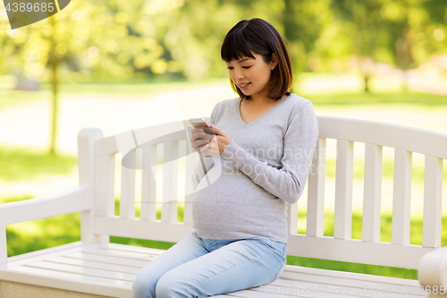 Image of happy pregnant asian woman with smartphone at park