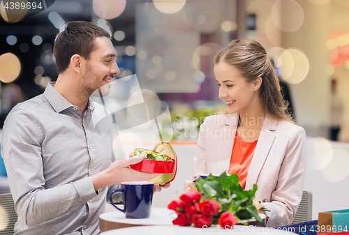 Image of happy couple with present and flowers in mall