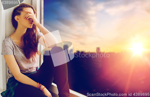 Image of unhappy teenage girl sitting on windowsill