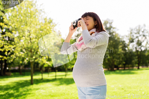 Image of happy pregnant asian woman with camera at park