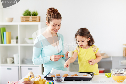 Image of happy mother and daughter eating cookies at home