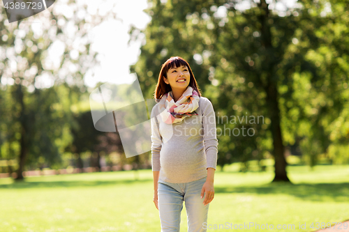 Image of happy pregnant asian woman walking at park