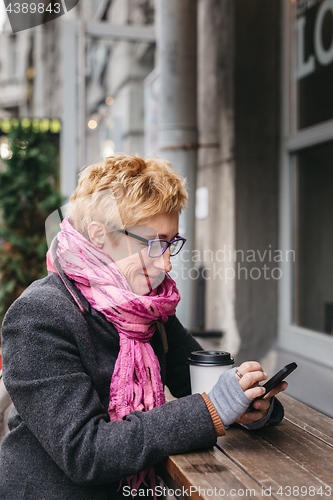 Image of Woman browsing smartphone in outside cafe