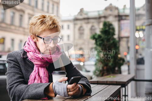 Image of Woman browsing phone in outside cafe