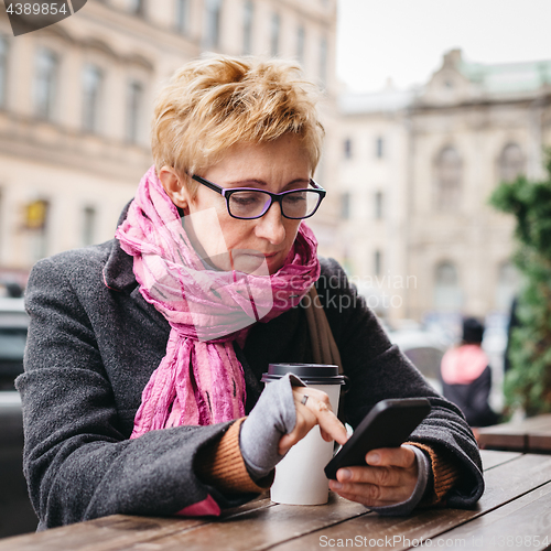 Image of Woman browsing smartphone in outside cafe