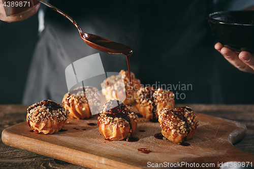 Image of Decorating delicious homemade eclairs with chocolate and peanuts